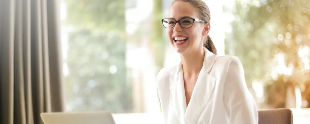 Eine lächelnde junge Frau in Ihrem Büro aus Glas, symbolisch für die Transparenz und klare Einblicke in einer offenen Unternehmenskultur. 